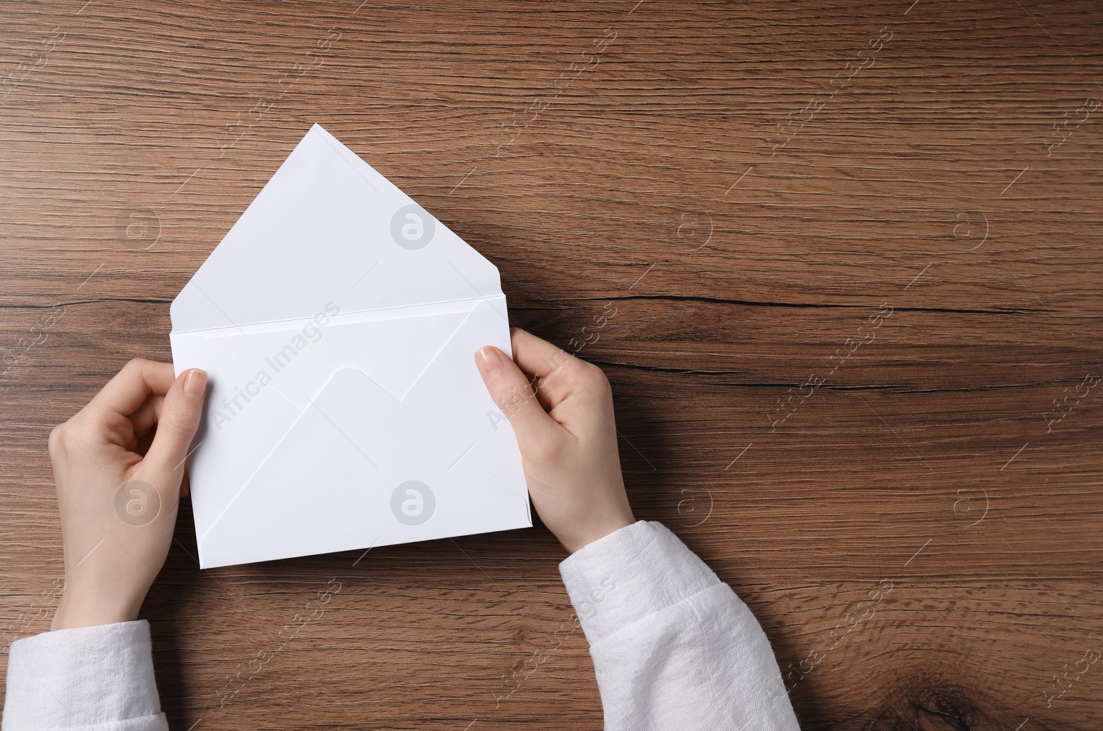 Photo of Woman holding letter envelope with card at wooden table, top view. Space for text