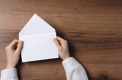 Photo of Woman holding letter envelope with card at wooden table, top view. Space for text