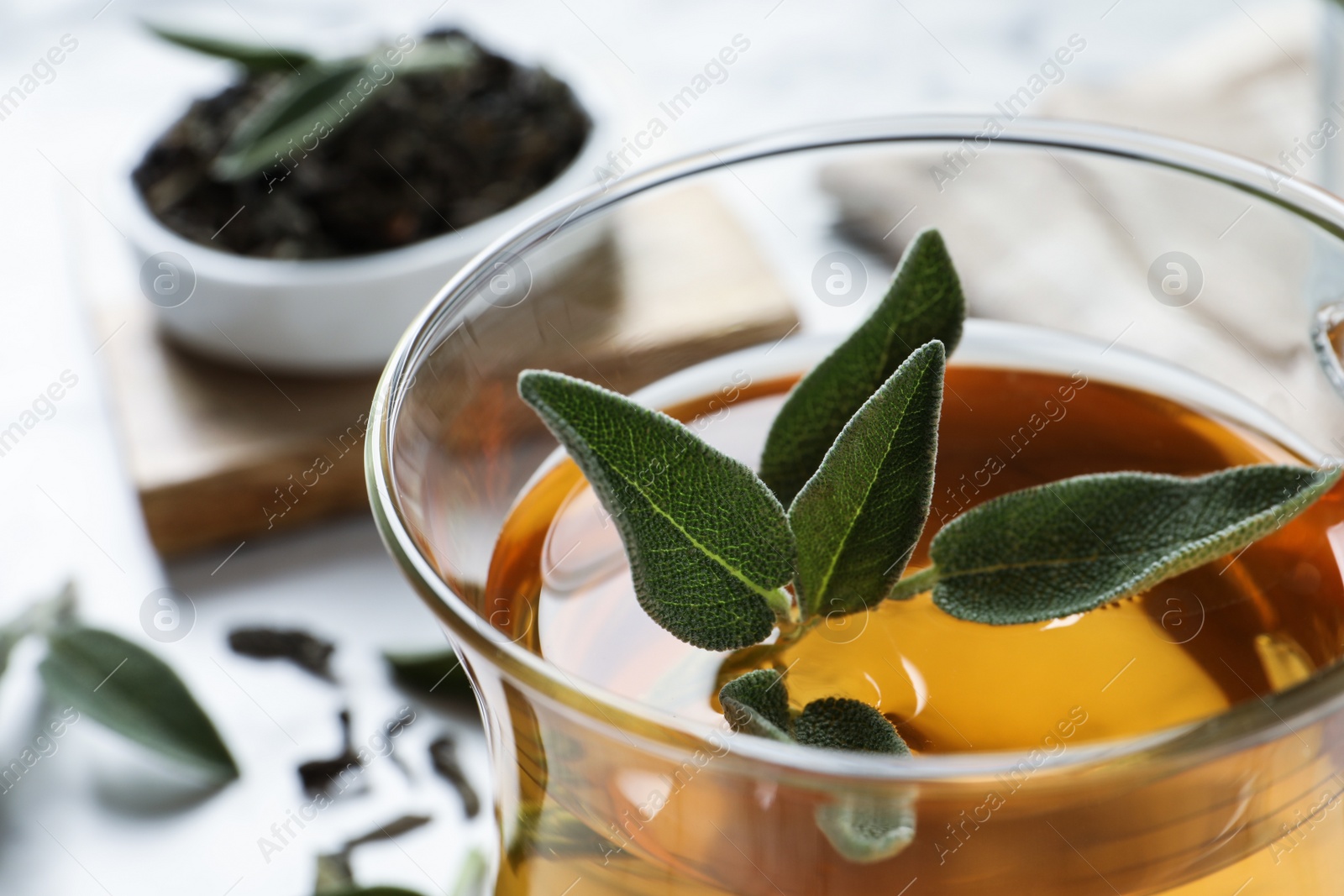 Photo of Cup of aromatic sage tea with fresh leaves on table, closeup