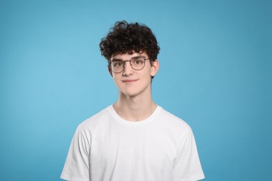 Portrait of cute teenage boy wearing glasses on light blue background