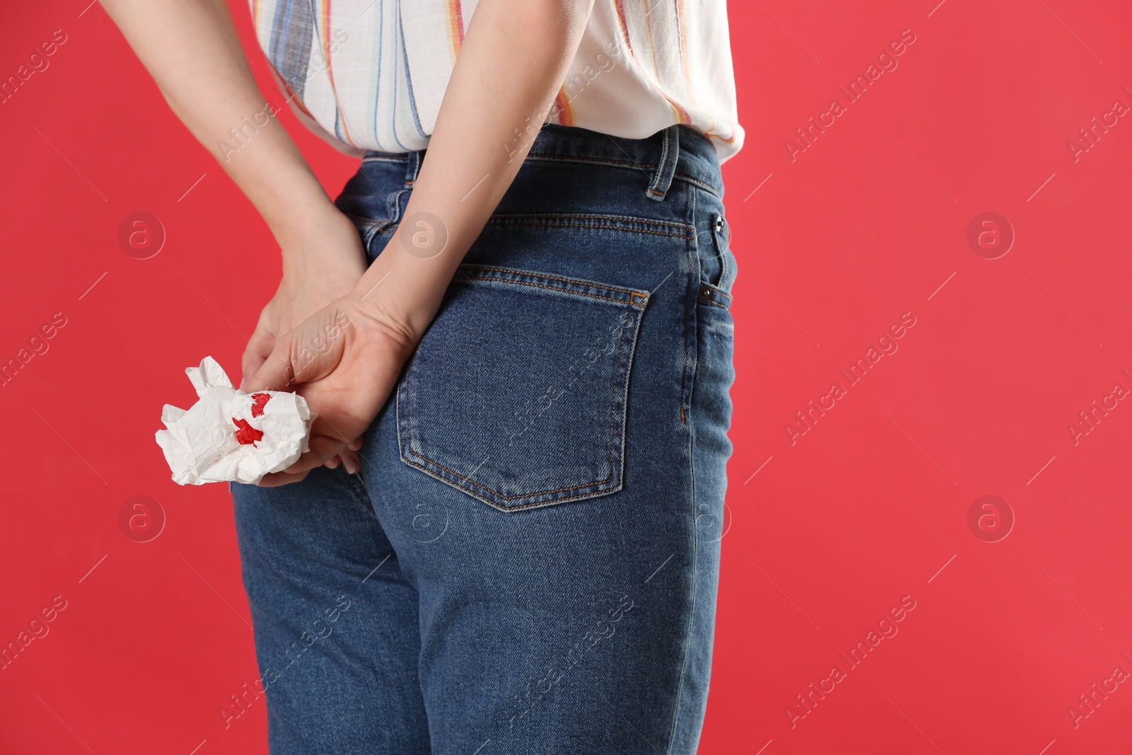 Photo of Woman holding toilet paper with blood stain on red background, closeup. Hemorrhoid concept