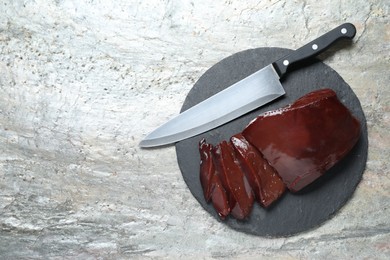Photo of Cut raw beef liver and knife on grey table, top view. Space for text