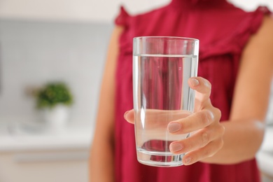 Photo of Woman holding glass with water in kitchen, closeup. Space for text