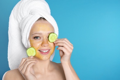 Photo of Beautiful woman holding cucumber slices near her face with natural mask against color background. Space for text