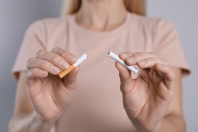 Photo of Woman with broken cigarette on light grey background, closeup. Stop smoking concept