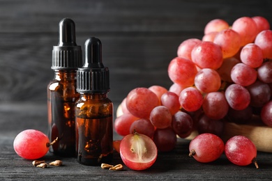 Photo of Organic red grapes, seeds and bottles of natural essential oil on black wooden table