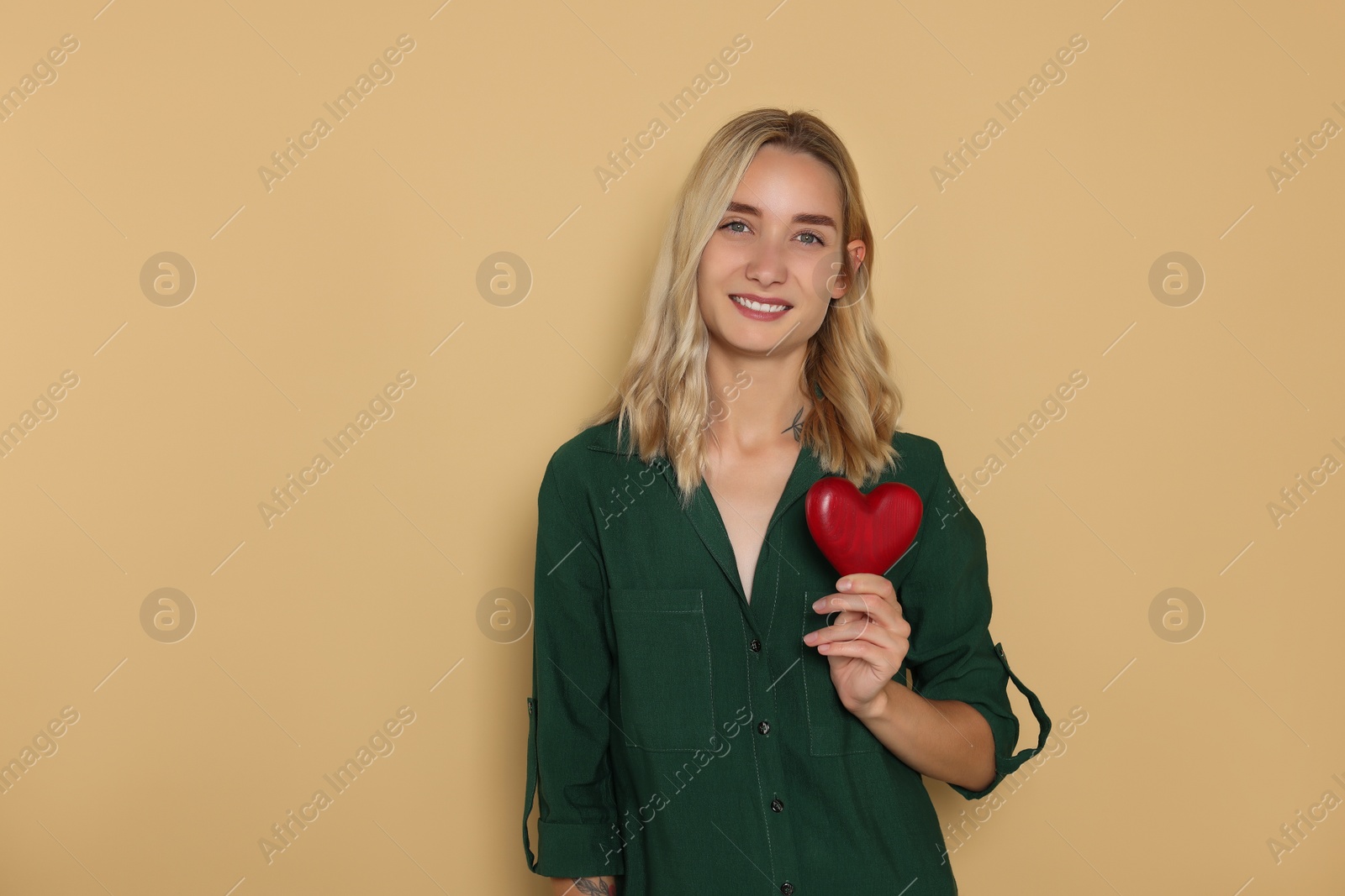 Photo of Happy volunteer holding red heart with hands on beige background. Space for text