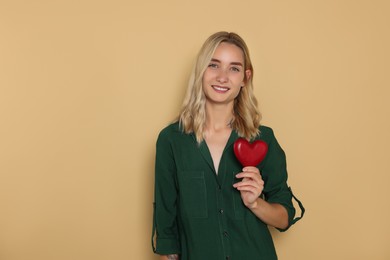 Photo of Happy volunteer holding red heart with hands on beige background. Space for text