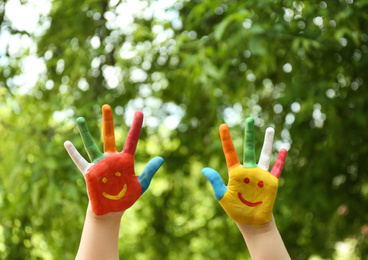 Photo of Kid with smiling faces drawn on palms in green park, closeup