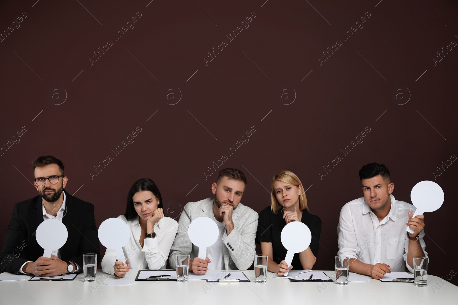 Photo of Panel of disappointed judges holding blank score signs at table on brown background. Space for text