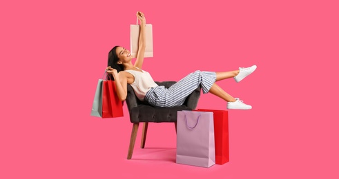 Photo of Beautiful young woman with paper shopping bags in armchair on pink background