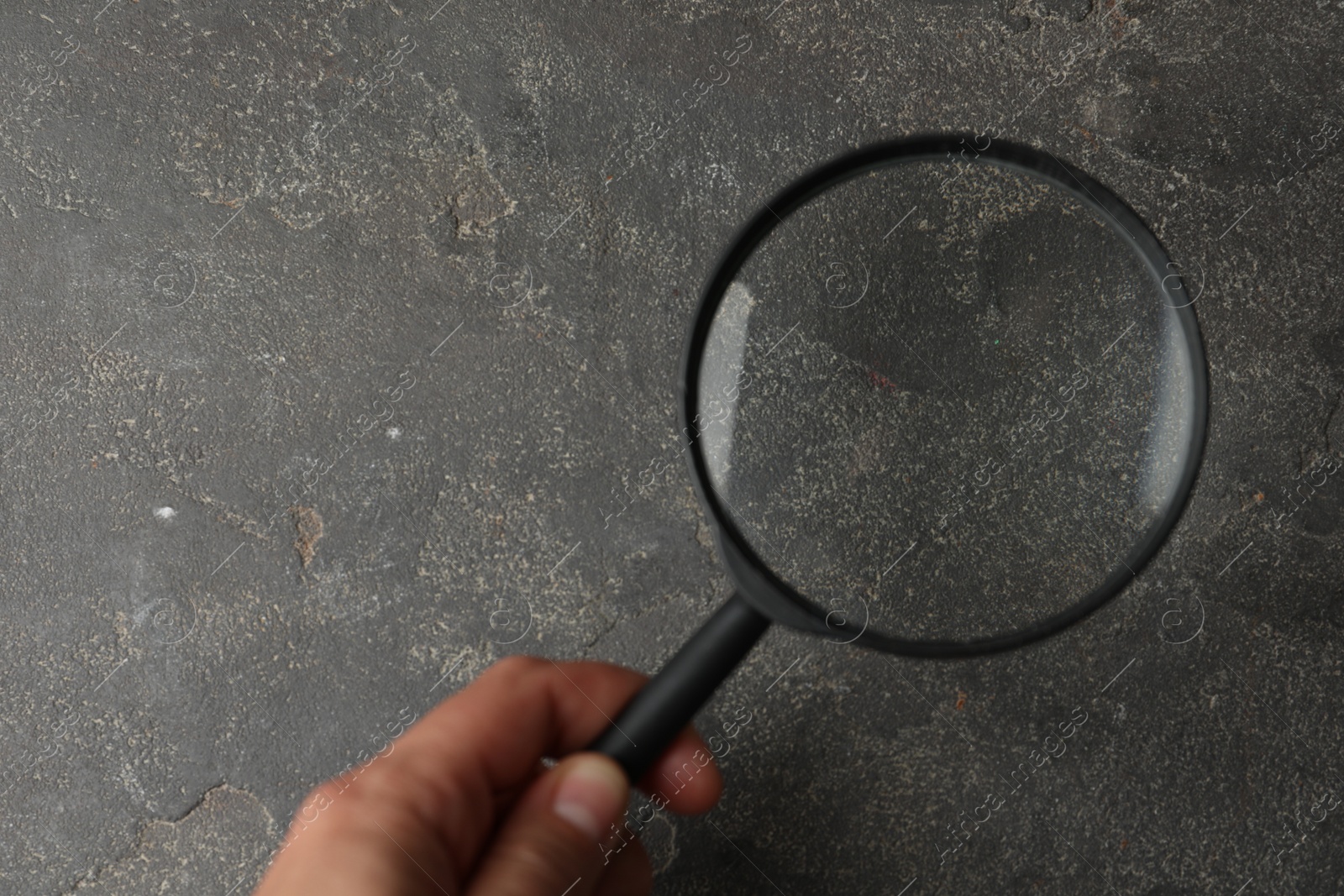 Photo of Closeup view of woman holding magnifier glass over grey stone table, space for text. Find keywords concept