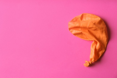 Photo of Orange deflated balloon on color background, top view with space for text