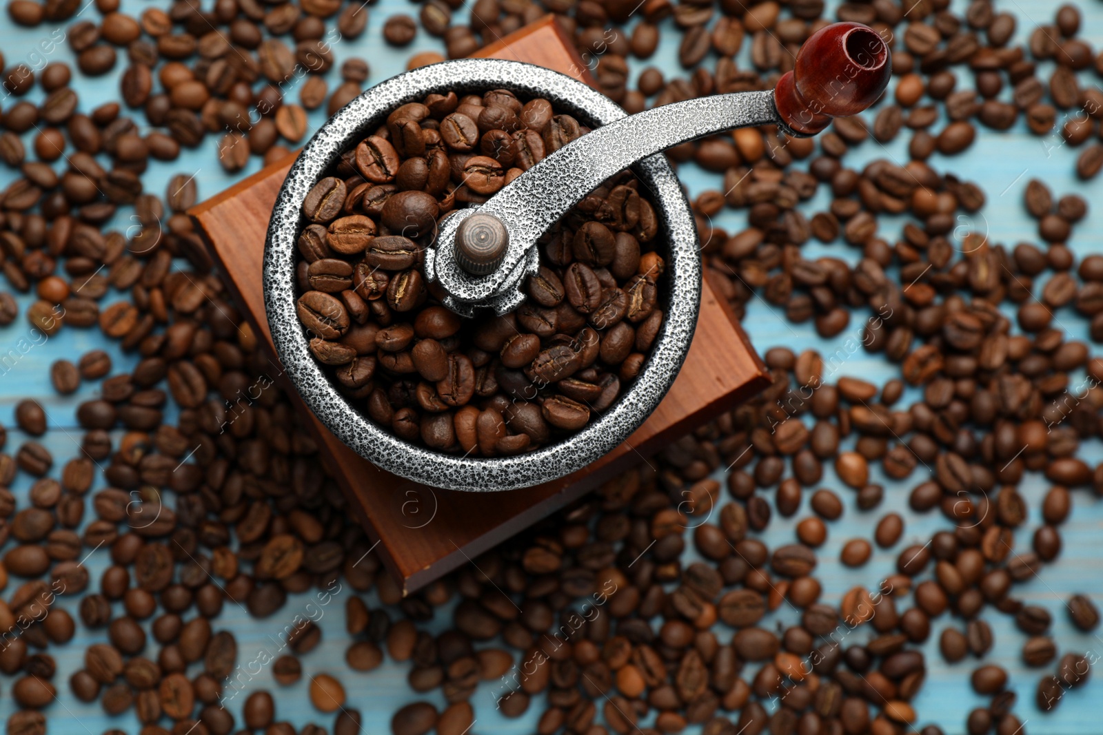 Photo of Vintage manual coffee grinder with beans on light blue wooden table, flat lay