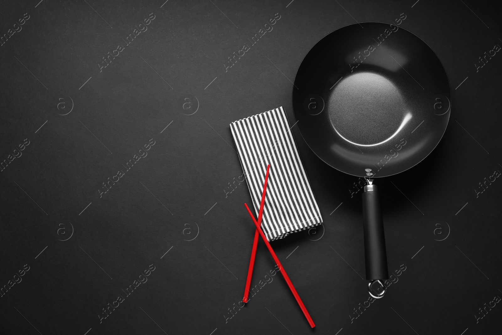 Photo of Empty iron wok and chopsticks on black table, flat lay. Space for text