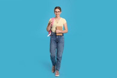Photo of Teenage girl with books and backpack on light blue background