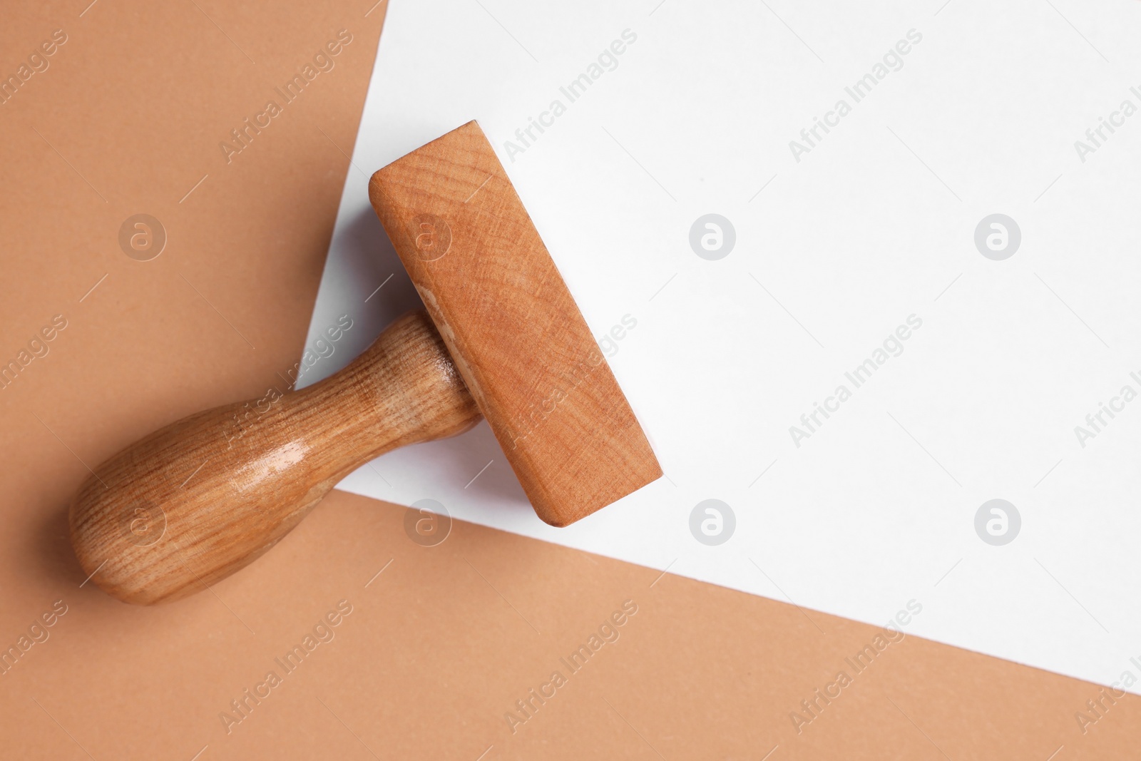 Photo of One wooden stamp tool and sheet of paper on light brown background, top view. Space for text