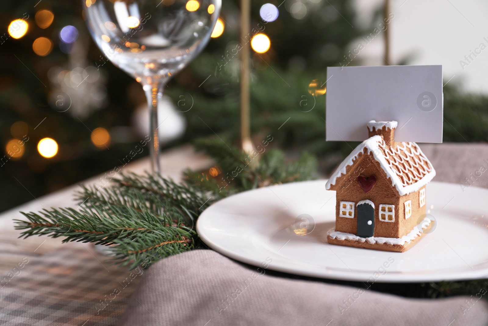 Photo of Festive place setting with beautiful dishware and gingerbread house card holder for Christmas dinner on checkered tablecloth, closeup. Space for text