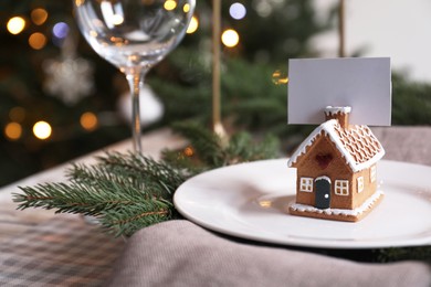 Festive place setting with beautiful dishware and gingerbread house card holder for Christmas dinner on checkered tablecloth, closeup. Space for text