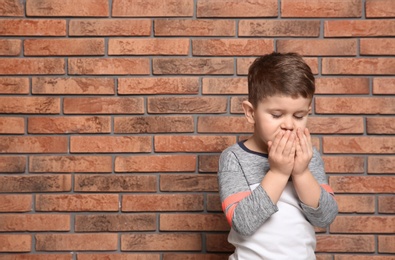 Cute boy suffering from cough near brick wall. Space for text