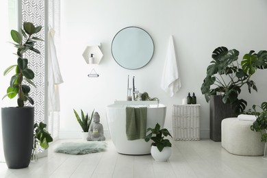 Photo of Stylish bathroom interior with modern tub, houseplants and beautiful decor. Home design