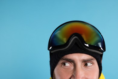Winter sports. Man in ski goggles on light blue background, closeup with space for text