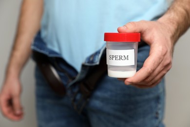 Photo of Donor with unzipped pants holding container of sperm, closeup