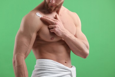 Man applying moisturizing cream onto his shoulder on green background, closeup