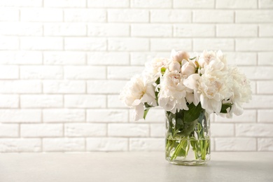 Vase with beautiful blooming peonies on table near brick wall