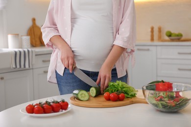 Photo of Young pregnant woman preparing vegetable salad at table in kitchen, closeup. Healthy eating