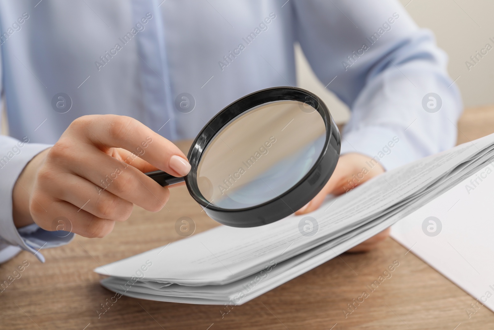 Photo of Woman looking at document through magnifier at wooden table, closeup. Searching concept