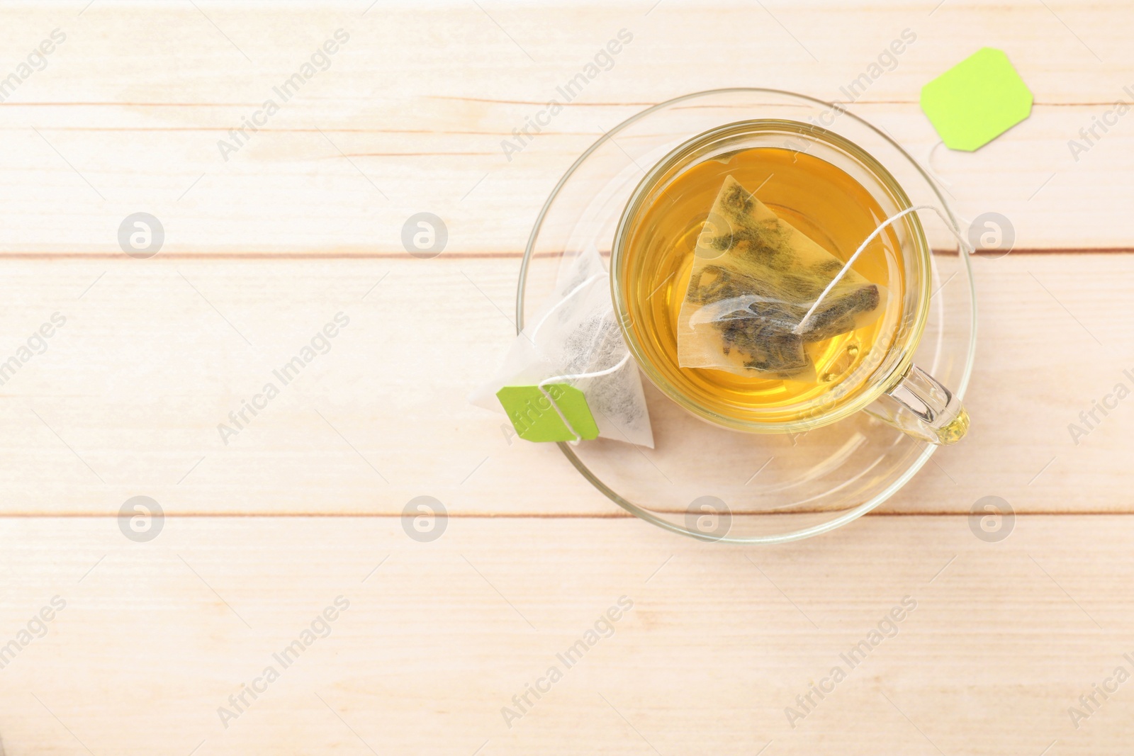 Photo of Tea bag in glass cup on light wooden table, top view. Space for text