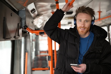 Photo of Young man listening to music with headphones in public transport. Space for text