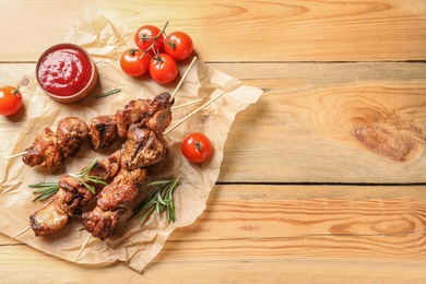 Photo of Delicious barbecued meat served with sauce and garnish on wooden background, top view. Space for text