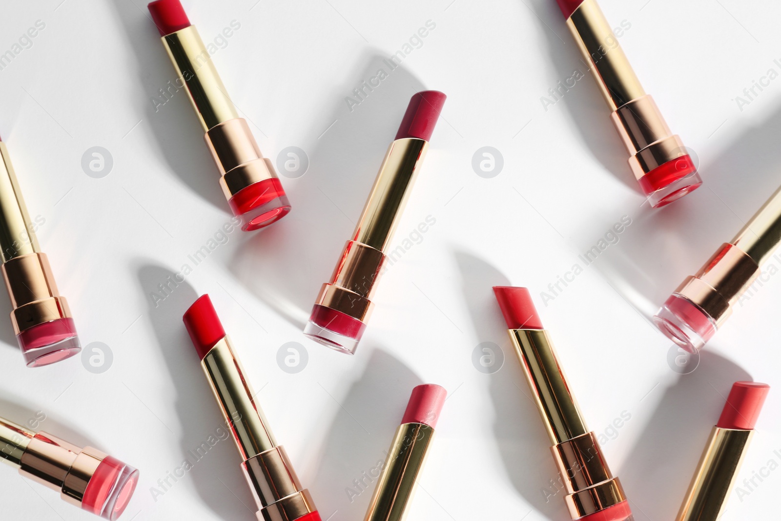 Photo of Set of bright lipsticks in gold tubes on white background, flat lay