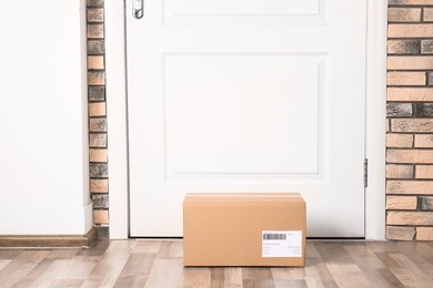 Photo of Cardboard parcel box on floor near apartment entrance. Mockup for design