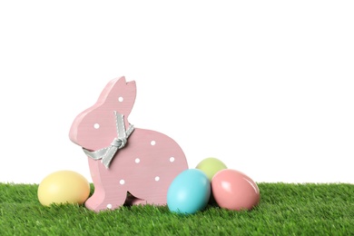 Cute wooden Easter bunny and dyed eggs on green grass against white background, space for text