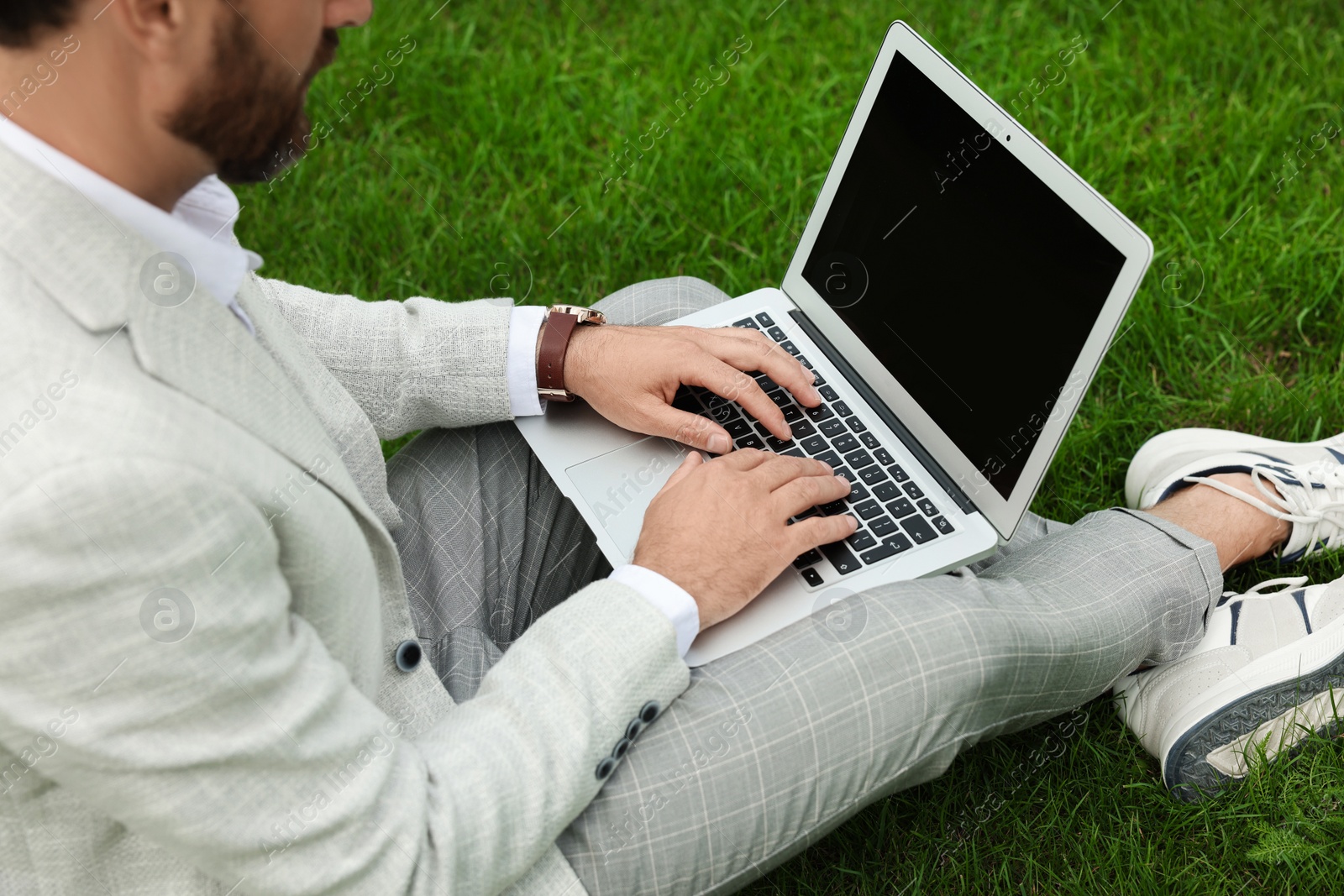 Photo of Businessman with laptop on green grass outdoors, closeup