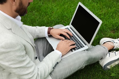 Photo of Businessman with laptop on green grass outdoors, closeup