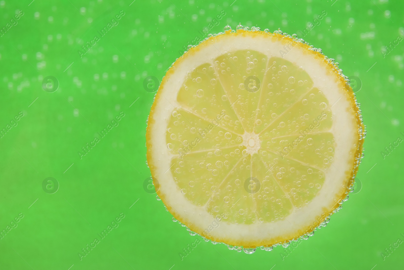 Photo of Slice of lemon in sparkling water on green background, space for text. Citrus soda
