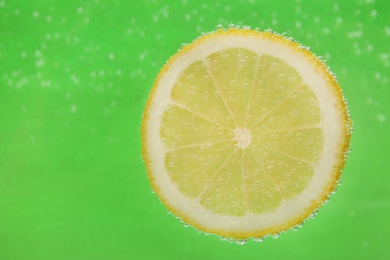 Photo of Slice of lemon in sparkling water on green background, space for text. Citrus soda