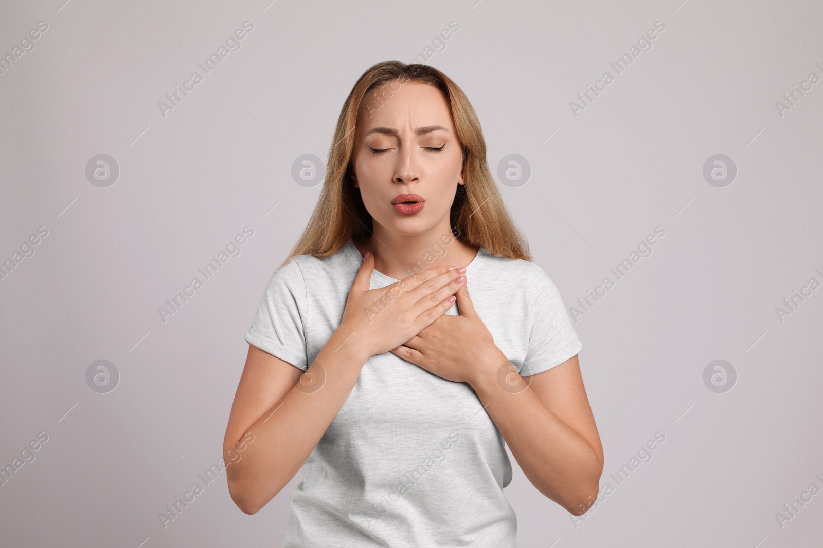 Photo of Young woman suffering from pain during breathing on light grey background