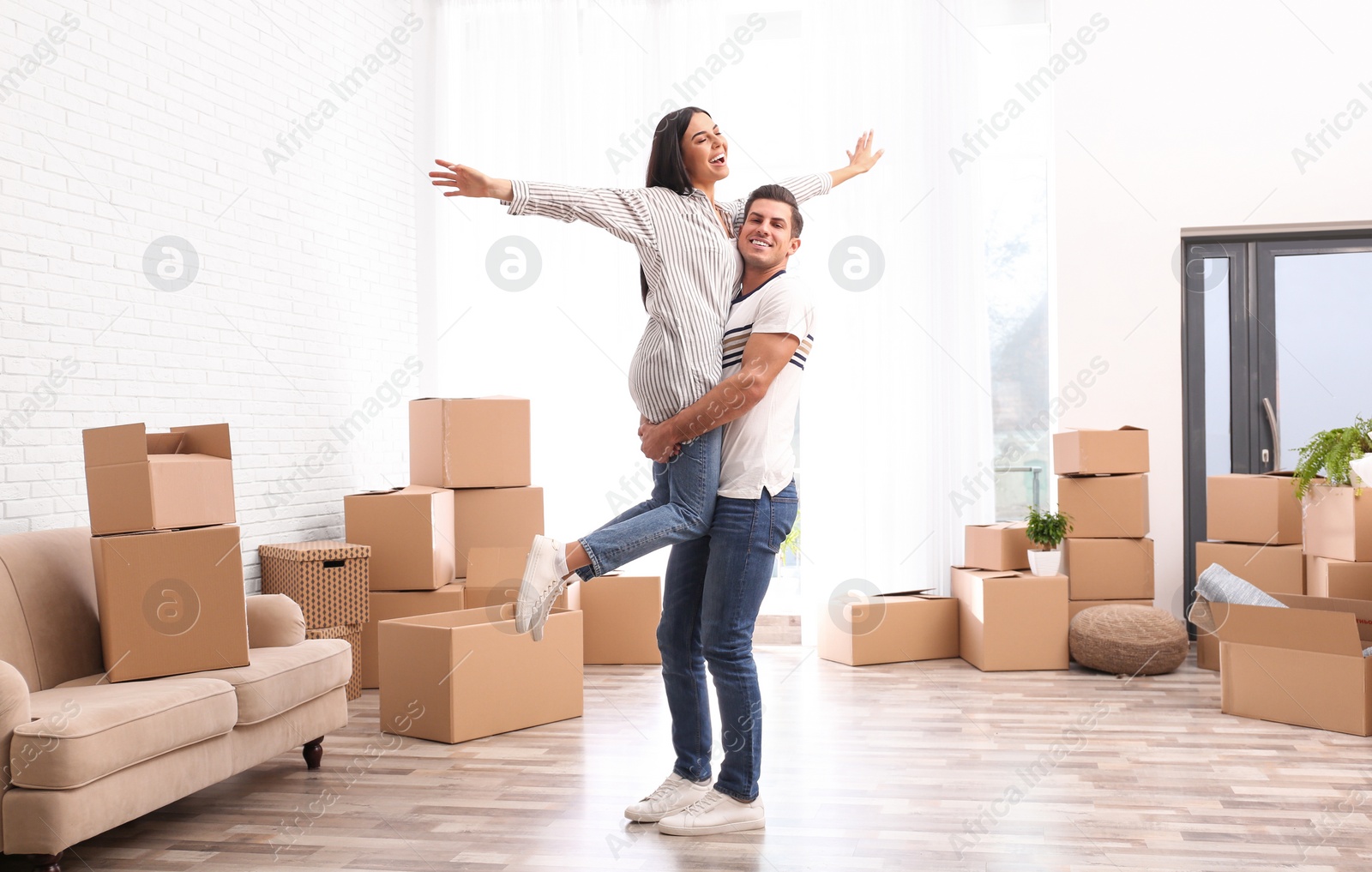 Photo of Happy couple having fun in room with cardboard boxes on moving day