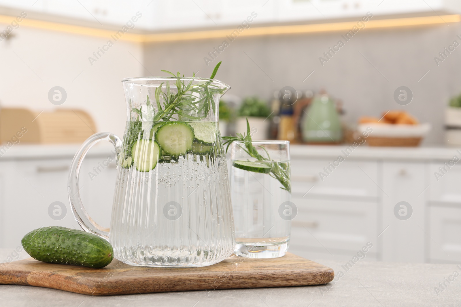 Photo of Refreshing cucumber water with rosemary and vegetable on table in kitchen. Space for text