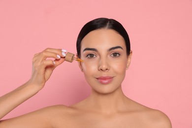 Photo of Young woman applying essential oil onto face against pink background