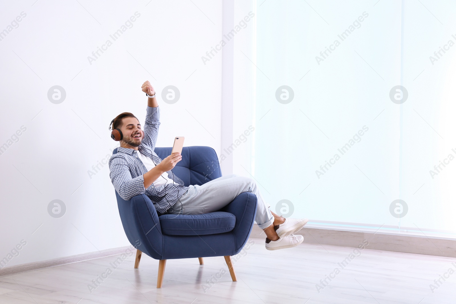 Photo of Handsome young man listening music in armchair indoors. Space for text