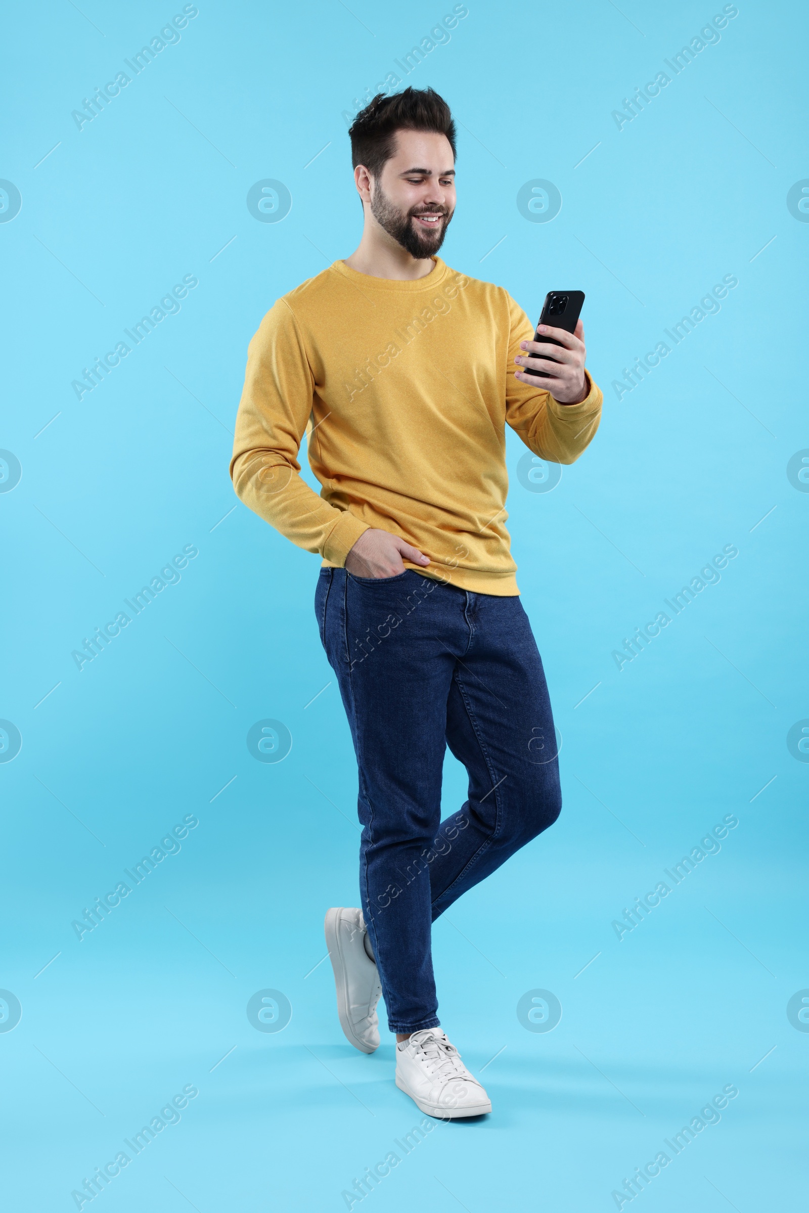 Photo of Happy young man using smartphone on light blue background