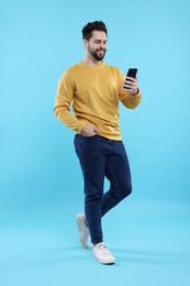 Happy young man using smartphone on light blue background