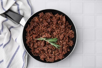 Photo of Fried ground meat in frying pan and rosemary on white tiled table, top view