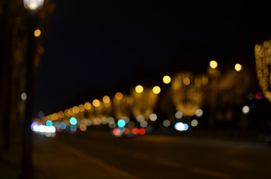 Photo of Blurred view of street with beautiful lights on trees and cars at night. Bokeh effect